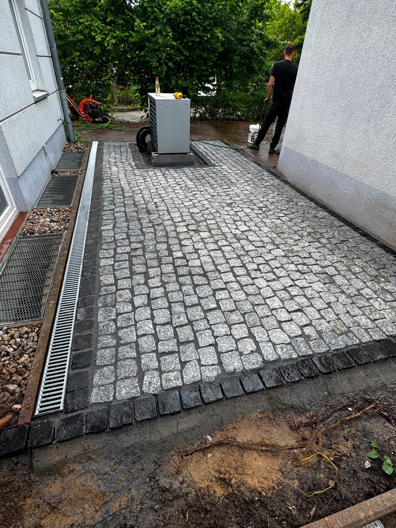 Echtes Kundenprojekt: frisch verlegtes Granit-Kleinpflaster mit Entwässerungsrinne am Haus